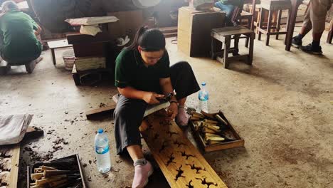 woman having several tools and carving a design on a pi;;ar wood in thailand