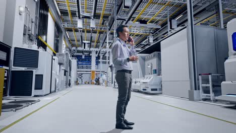 full body side view of an asian male professional worker standing at factory digitalization, he is speaking with someone in the phone and moving his left hand