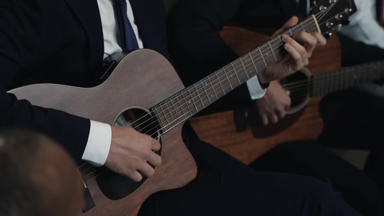 공식적인 음악적 공연을 강조하면서 어쿠스틱 기타를 연주하는 슈트 남자