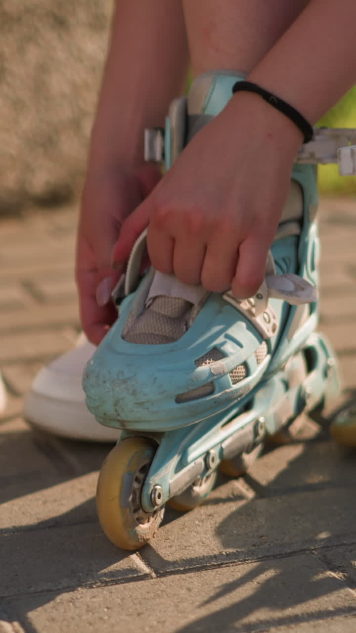 Partial view of individual adjusting roller skate strap on right leg while wearing black wristband, second roller skate is lying by in background, white sneakers placed nearby the other side