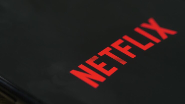 Smartphone with various app icons, finger touching Netflix icon