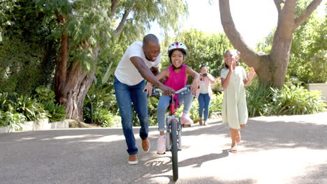 father teaching daughter to ride bicycle, family enjoying outdoor activity together
