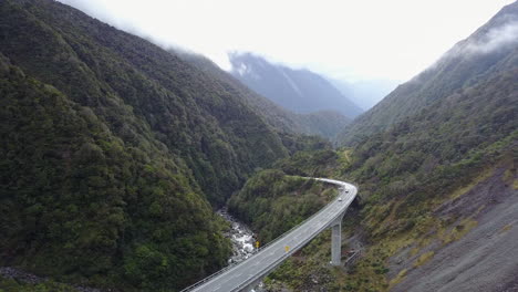 aerial tracking shot of cars on a road with mountain forest and rocky cliff face