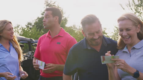 mature and mid adult couples standing by golf buggy checking score cards together