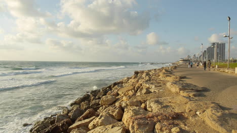 Coastal-Boardwalk-Along-the-Beach,-Rocky-Waves-Crashing,-Blue-Cloudy-Sky