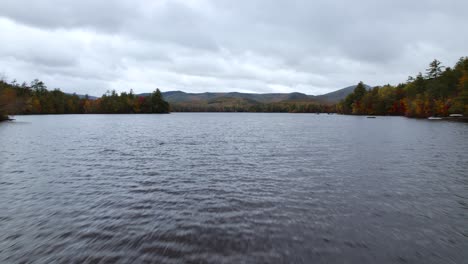 drone flying low over lake and waterfall on moody overcast day in new england