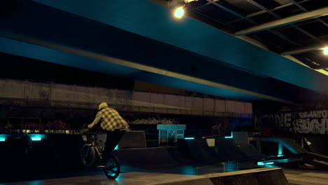 Young-man-practicing-bmx-bicycle-in-ramp-at-night-urban-skate-park.