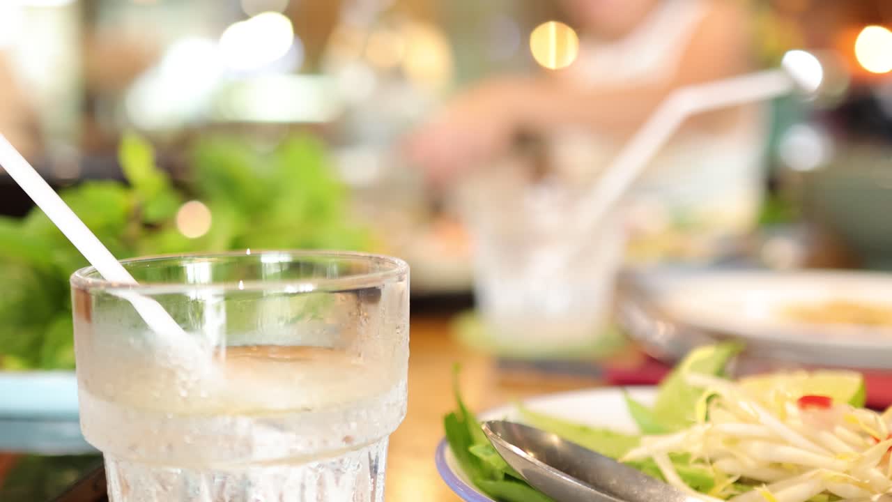 A close-up view of a water glass on a restaurant table, with blurred background activity