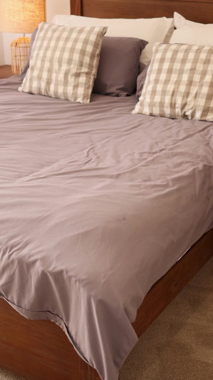 Uma pessoa arruma travesseiros em uma cama bem arrumada em um quarto aconchegante com iluminação suave.