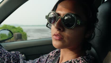 close-up shot of a young indian woman driving a car with stylish sunglasses