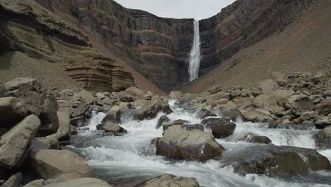 A-river-flowing-strongly-over-rocks-with-a-spectacular-waterfall-in-the-background