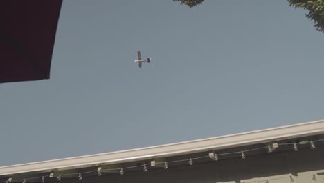 small plane flies over suburban home through clear blue sky