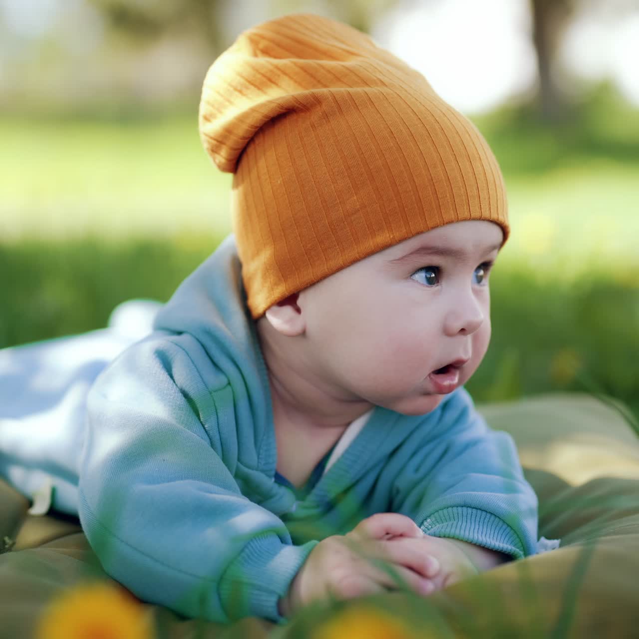 Half a year old toddler looks around with interest. Adorable child resting on the mattress outside in the nature