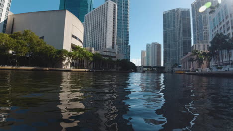 desde un pequeño bote como es filmado viaja por las aguas tranquilas de las vías fluviales de miami en un día soleado con altos edificios y palmeras por todas partes