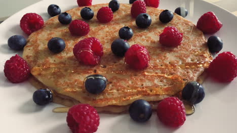 Goldener-Ahornsirup-Wird-über-Einen-Stapel-Pfannkuchen-Mit-Beeren-Gegossen