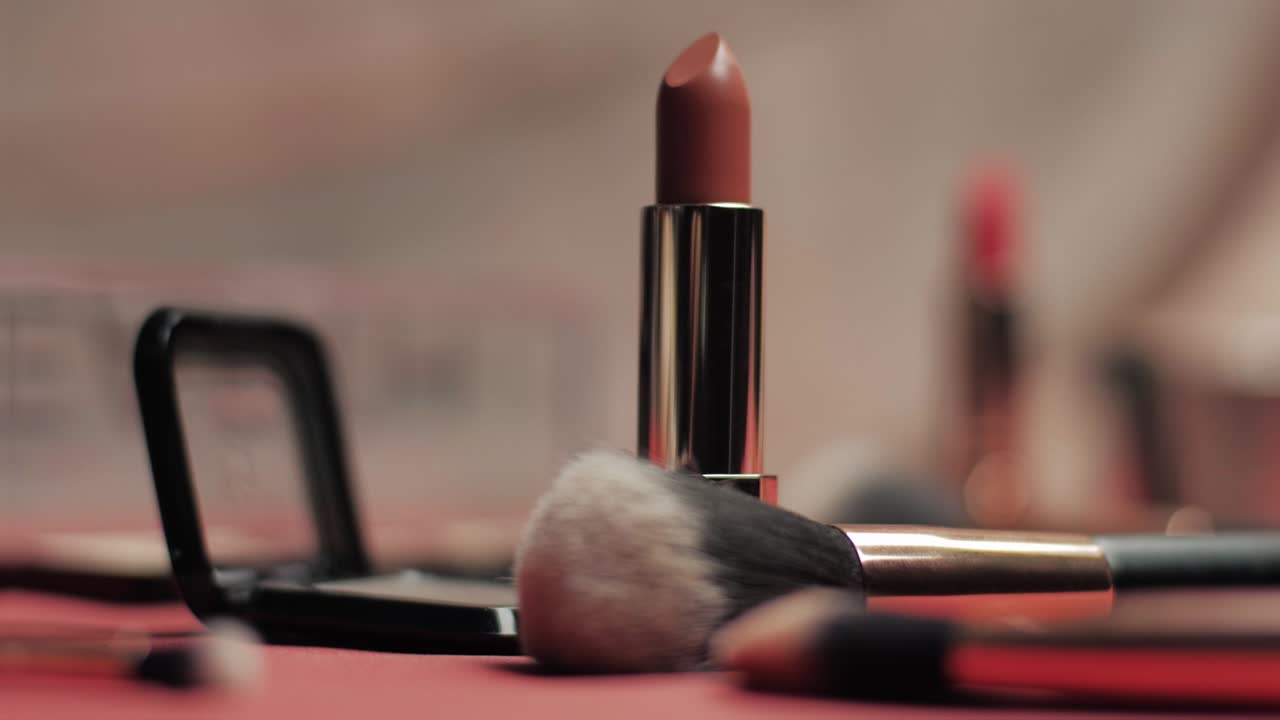 Close-up shot of a nude lipstick standing upright among soft makeup brushes and eyeshadow palettes in a warm, elegant beauty setting