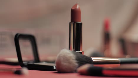close-up shot of a nude lipstick standing upright among soft makeup brushes and eyeshadow palettes in a warm, elegant beauty setting