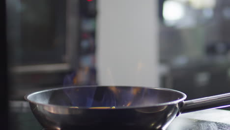 chef tossing vegetables in pan while flambeing