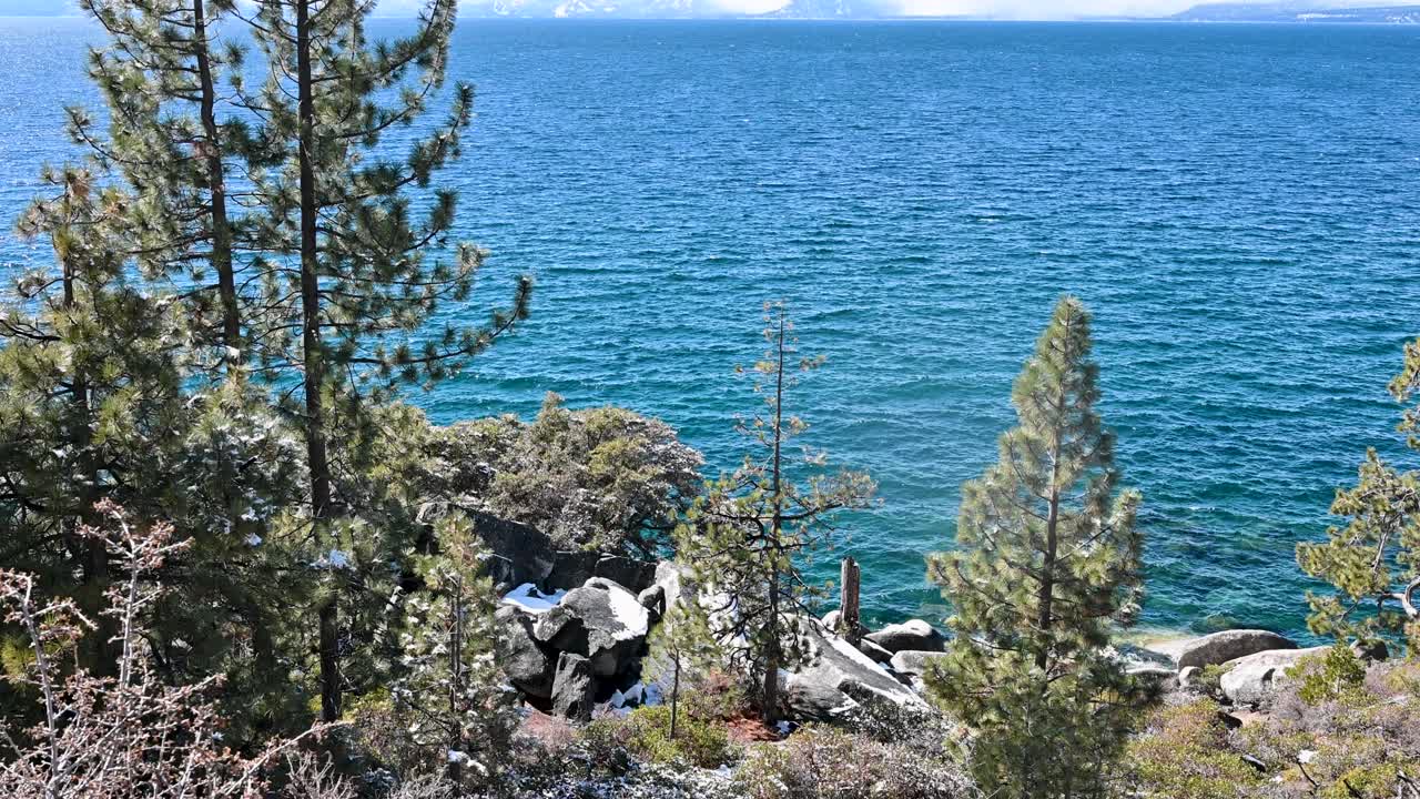 Vibrant turquoise mountain lake with rocky shoreline and evergreen trees under clear skies