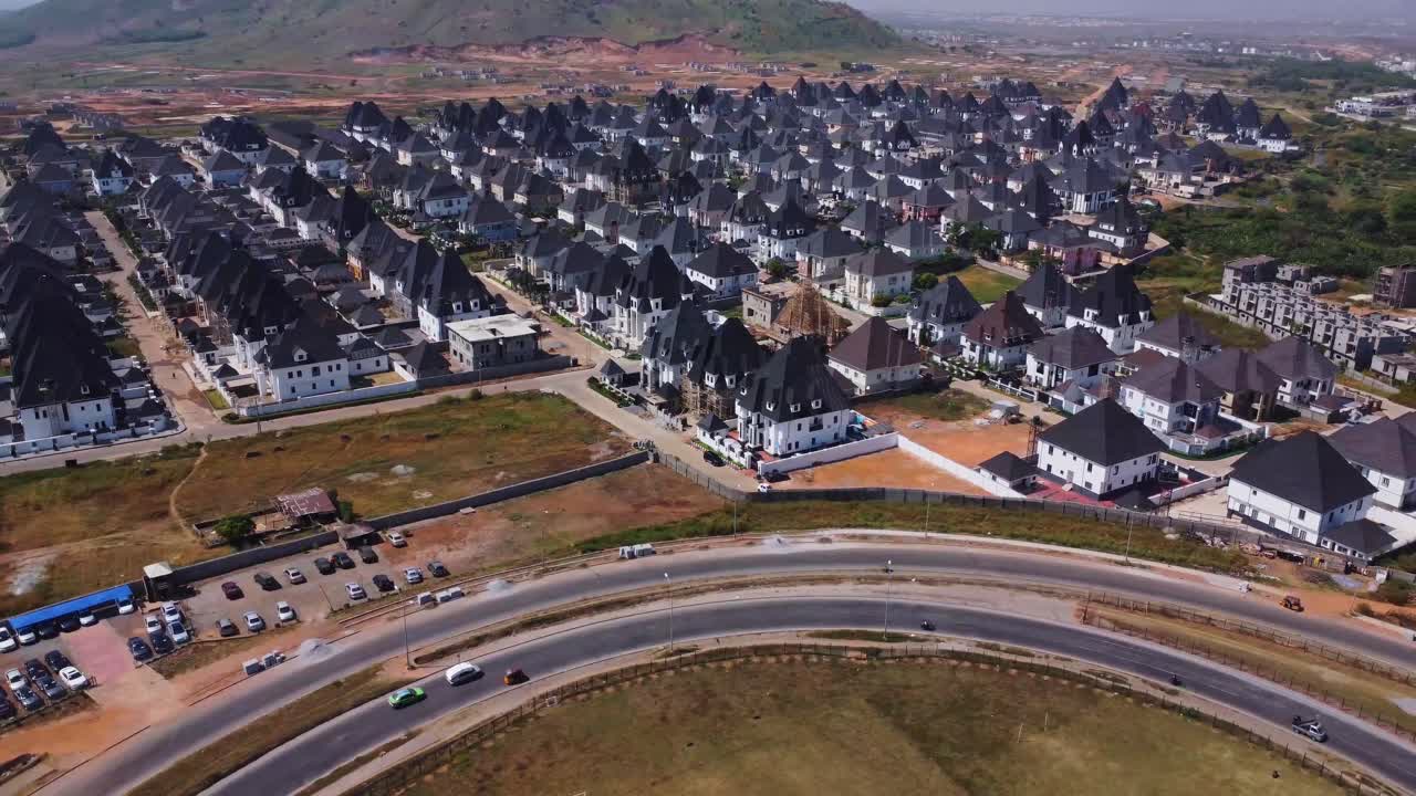 High angle pan of a busy freeway adjacent to a large and wealthy suburban neighborhood in Abuja, Nigeria