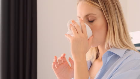 una mujer rubia pensativa bebiendo café en casa.