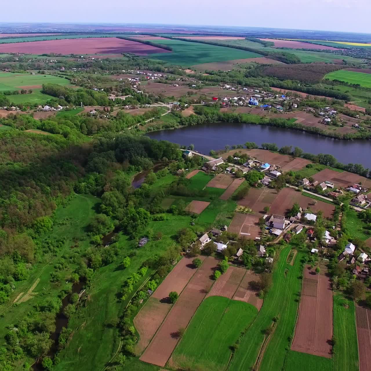 Large village locating at the bank of the river. Agricultural farmlands and green forests surrounding the rural area. Top view