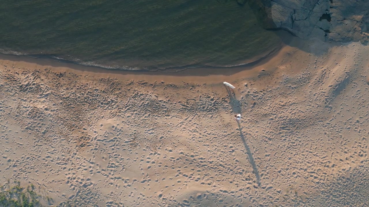 En mann går langs en sandstrand med hunden sin under solnedgangen, fanget ovenfra