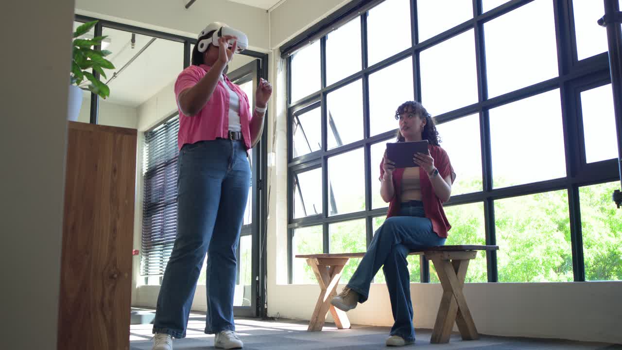 Donne afroamericane che indossano un visore VR bianco esplorano l'interfaccia utente in uno studio mentre una collega prende appunti su un tablet