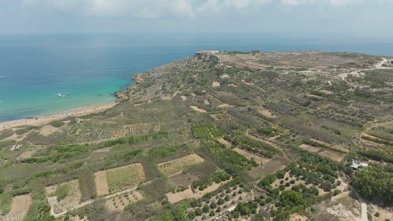 imágenes de drones de alta definición de una playa tranquila con aguas cristalinas, rodeada de terreno accidentado y barcos esparcidos en la distancia y el campo en el fondo