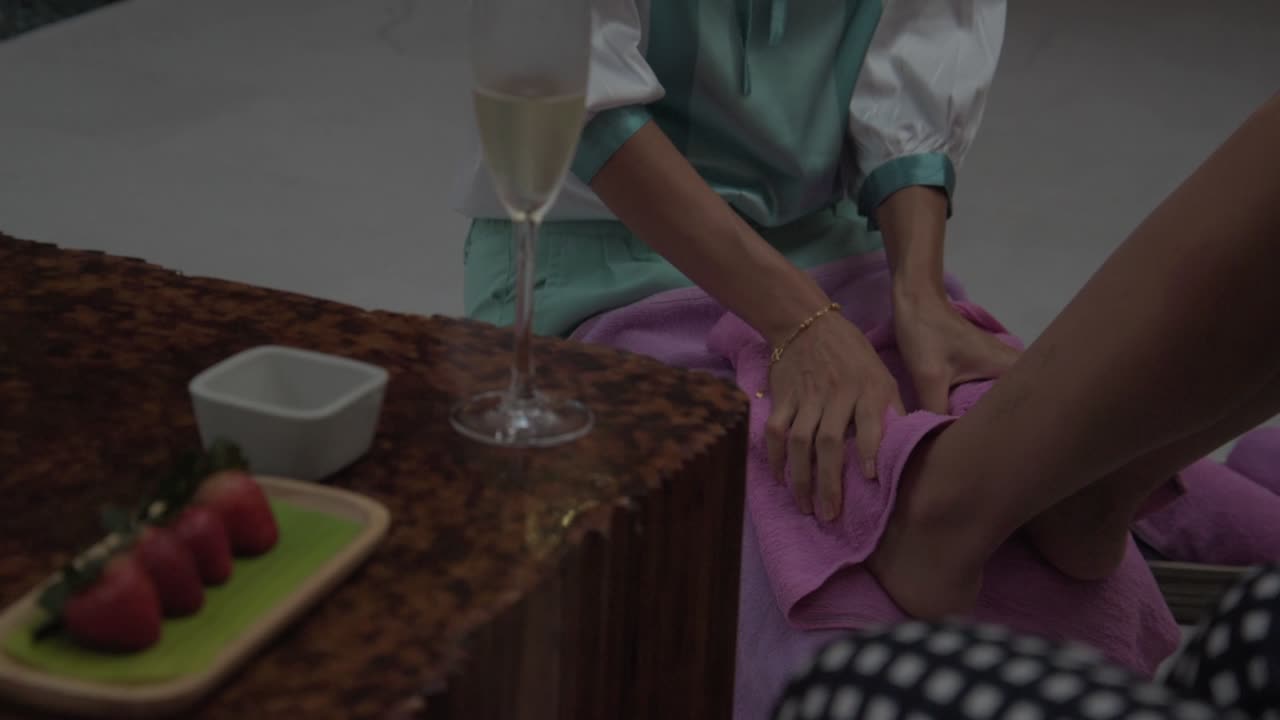 Una massaggiatrice che esegue un massaggio alle gambe, fragole e un bicchiere di champagne su un tavolo di legno