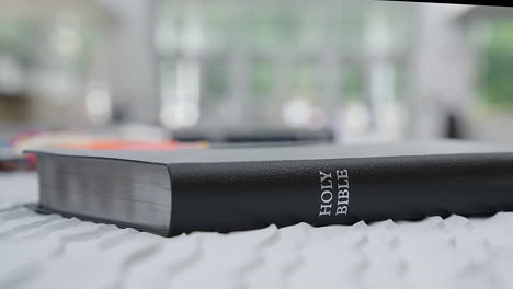 black leather holy bible rests on white bedding with soft, natural morning window light
