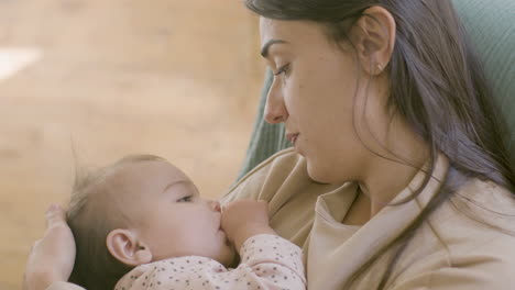 close up shot of an adorable baby girl sucking her thumb and falling asleep while her mother holding her, singing a lullabay and stroking her hair gently