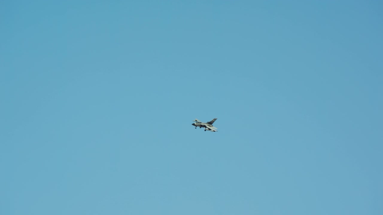 Militært jagerfly daler i slowmotion mod en klar blå himmel, forbereder sig på landing med landingsstellet nede under en dagflyvning.
