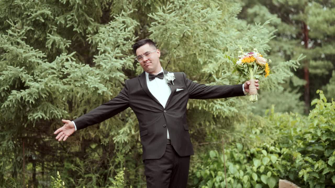Groom poses with bouquet before switching to a funny arms-out pose among trees