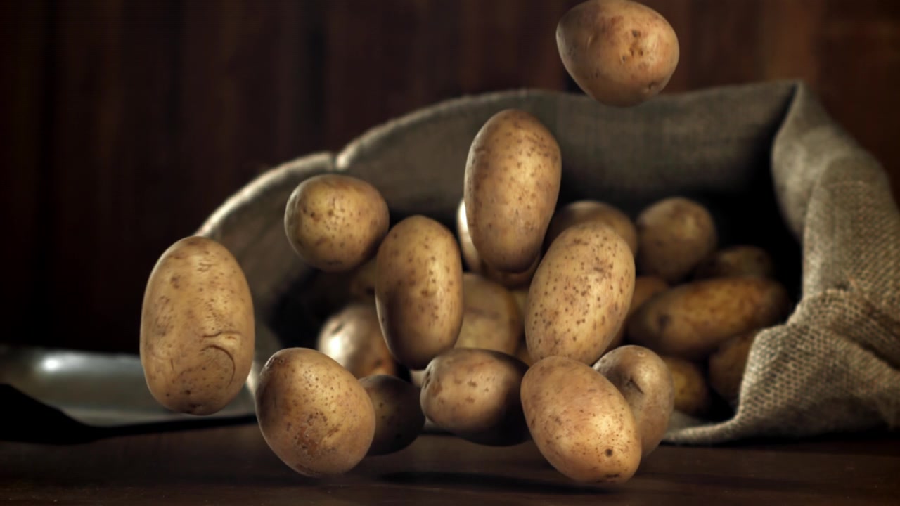 Patate fresche e crude che cadono al rallentatore su un tavolo di legno.