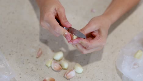 close-up of hands peeling garlic cloves on a light kitchen countertop. natural lighting, steady camera, focused on culinary preparation