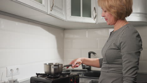 mature woman preparing to cook, carefully placing pot on gas burner while checking if flame is lit, standing in bright kitchen, focused and ready to start cooking process