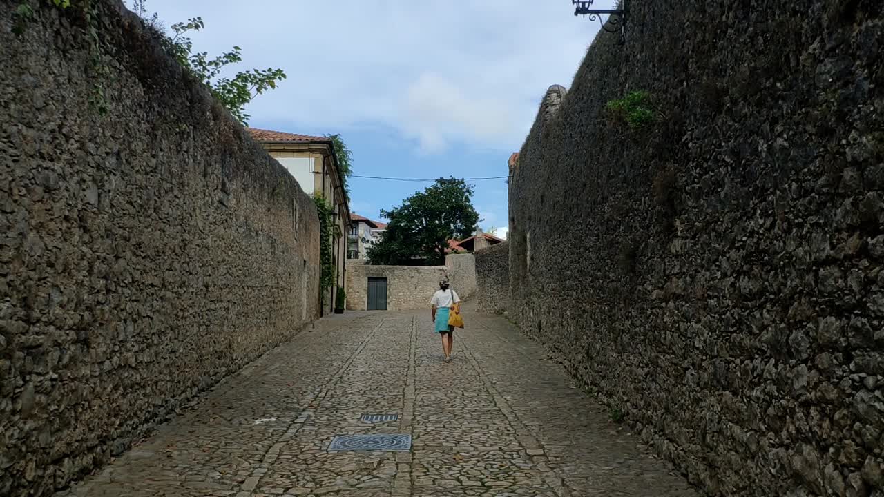 Woman walks alone on cobbled Santillana Del Mar street between stone walls