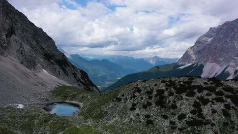 Austrian-Alps-pond-aerial-orbit-clouds-blue-water