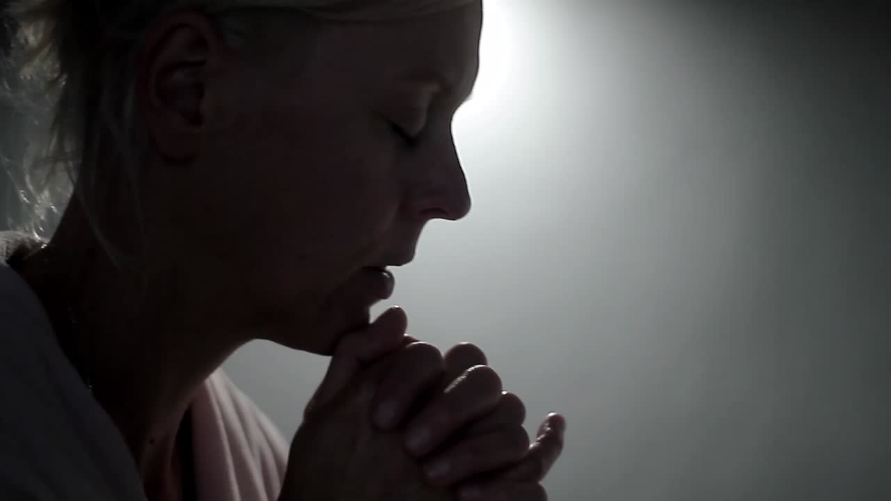 mujer rezando a dios con las manos juntas sobre fondo gris metrajes