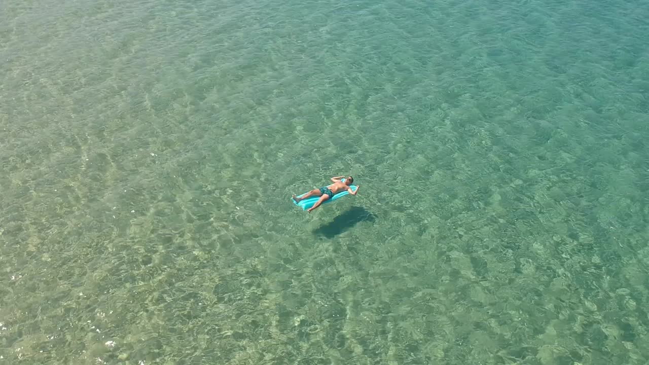 Guy floats on a inflatable mattress in the Aegean sea in town of Skala Sotiros Greece
