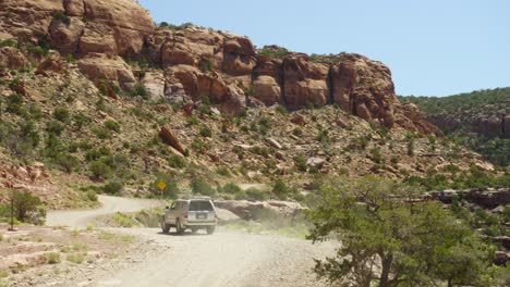 el vehículo suv conduce por el polvoriento camino de grava serpenteando a lo largo de los escarpados cañones de moab.
