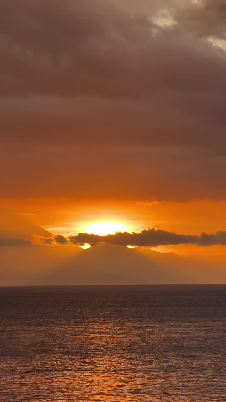 Dramatisk gylden solnedgang over havet med skyer og bjergsilhuet