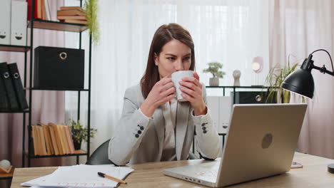 business woman drinking cup of warm hot coffee sits at table office workplace relax taking a break