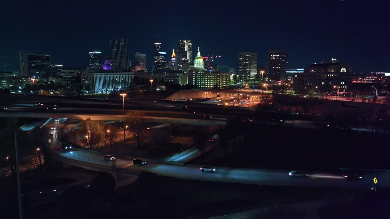 Traffic on highway and interstate in front of Downtown Skyline in american town. Night scene with Skyscrapers and high-rise buildings in background. Aerial Panorama wide shot.