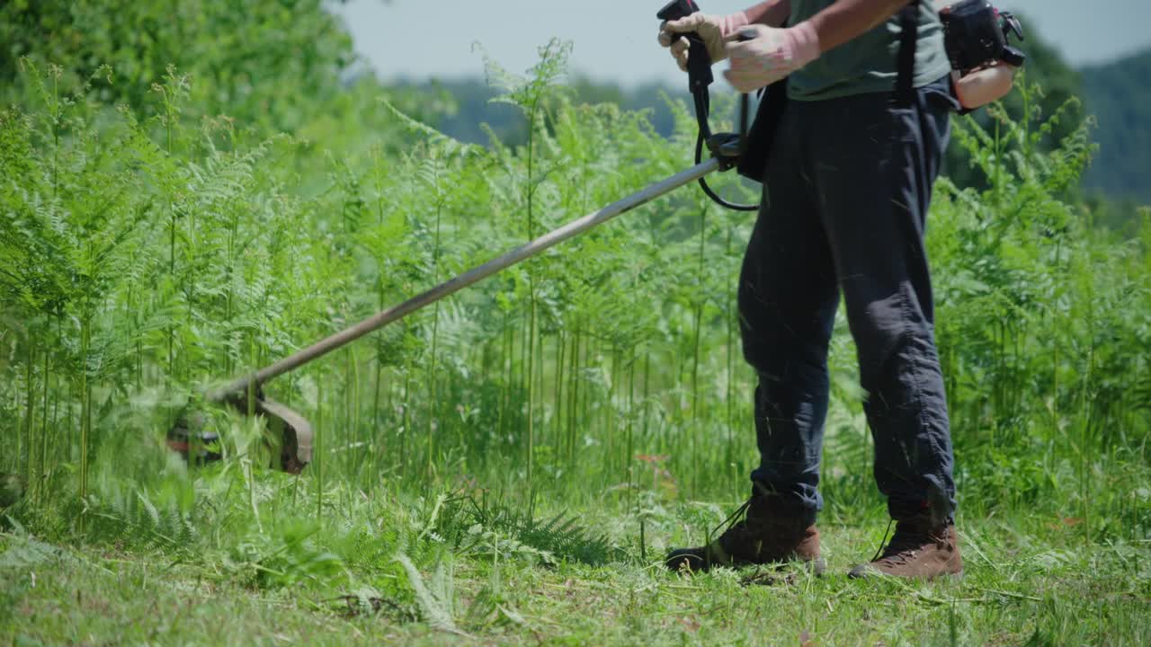 Man Trimming Overgrown Vegetation Using Gasoline-powered Brush Cutter. medium shot