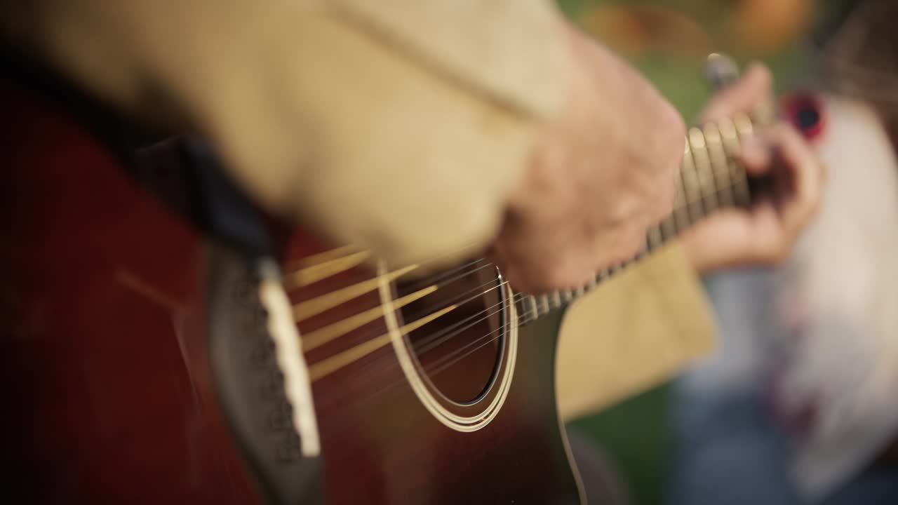A hobby guitarist plays on an acoustic guitar at a picnic in the park