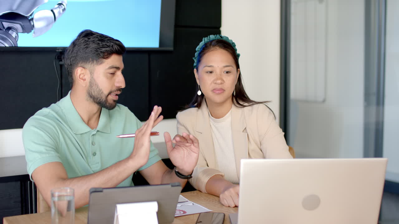 Discussing project, colleagues using tablet and laptop in modern office setting