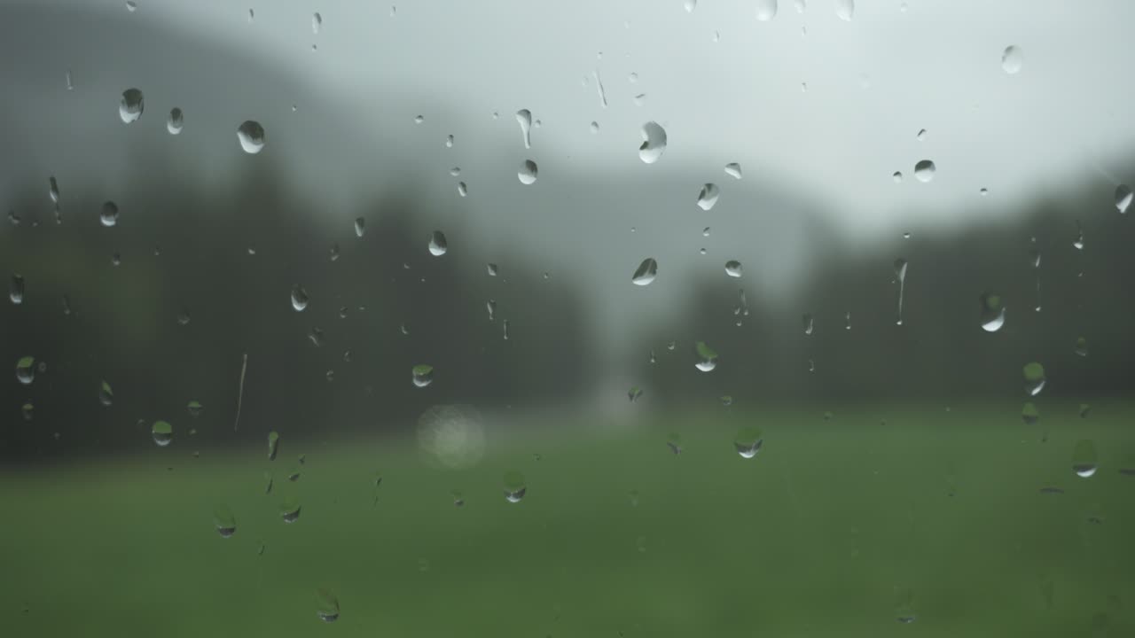 Rain drops on window glass with blurry nature background, static shot