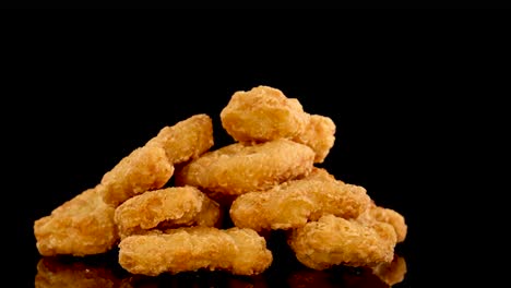 golden, crumbed chicken nuggets tumble and pile up on a glossy black surface under dramatic lighting, captured in slow motion with a static camera angle